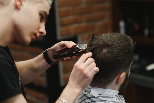 Making haircut look perfect. Young bearded man getting haircut by hairdresser while sitting in chair at barbershop. photo