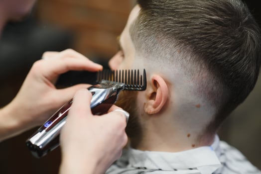 Making haircut look perfect. Young bearded man getting haircut by hairdresser while sitting in chair at barbershop. photo