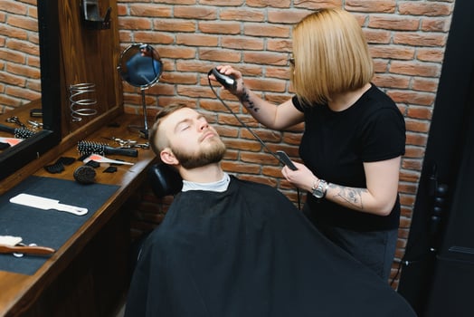Woman barber cutting hair to a bearded man. photo