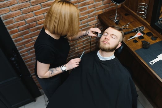 Skilled female barber cutting a beard of brunette adult guy in professional retro barbershop. photo