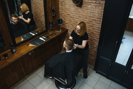 Stylish man sitting barber shop Hairstylist Hairdresser Woman cutting his hair Portrait handsome happy young bearded caucasian guy getting trendy haircut Attractive barber girl working serving client. photo