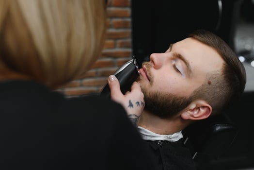 Barbershop or hairdresser concept. Woman hairdresser cuts beard with scissors. Man with long beard, mustache and stylish hair. Guy with modern hairstyle visiting hairdresser photo