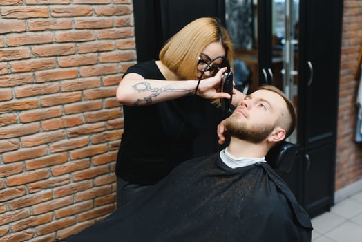 Young adult beautiful caucasian woman hairdresser cuts beard handsome man at modern barbershop Happy gay sitting chair men beauty salon. beard care. metrosexual. Female barber in black gloves serving photo