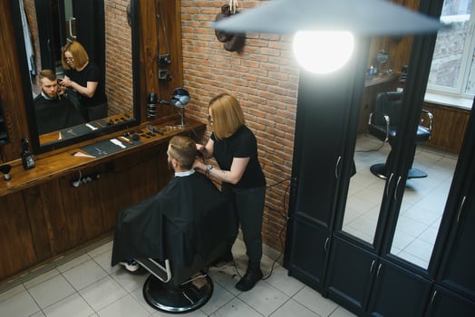 Stylish man sitting barber shop Hairstylist Hairdresser Woman cutting his hair Portrait handsome happy young bearded caucasian guy getting trendy haircut Attractive barber girl working serving client. photo