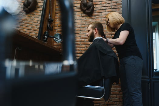 Stylish man sitting barber shop Hairstylist Hairdresser Woman cutting his hair Portrait handsome happy young bearded caucasian guy getting trendy haircut Attractive barber girl working serving client. photo