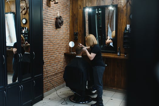 Stylish man sitting barber shop Hairstylist Hairdresser Woman cutting his hair Portrait handsome happy young bearded caucasian guy getting trendy haircut Attractive barber girl working serving client photo