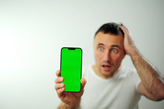 New technologies win adult phone green screen chromakey surprised and holding his hand behind his head he is very worried A white t-shirt and a white background for a man with dark hair photo