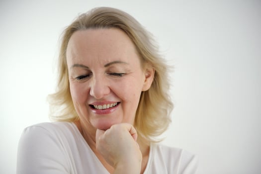 beautiful woman of shyness waiting on white background raised one shoulder to top screwed up her eyes a sincere modest smile a hand near her face tenderness femininity and yang fair hair middle age photo