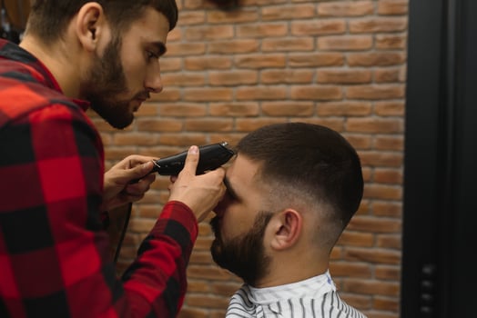Making haircut look perfect. Young bearded man getting haircut by hairdresser while sitting in chair at barbershop. photo