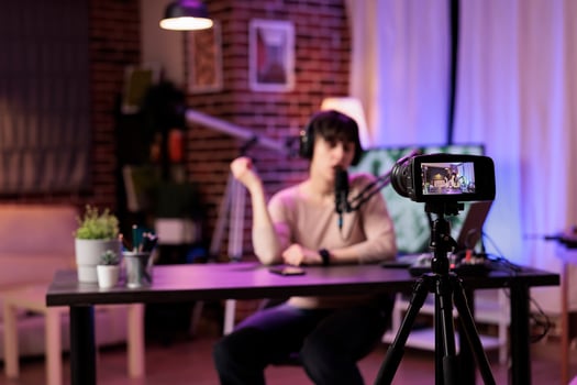 Focus shot on modern camera recording vlogger in blurry background talking about personal development subjects. Entertaining woman speaking on air during online show in studio photo