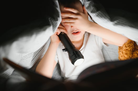Child reading book in bed. Kids read at night. Little boy with fairy tale books in bedroom . Education for young children. Bedtime story in the evening. Cute kid under blanket in dark room with lamp photo