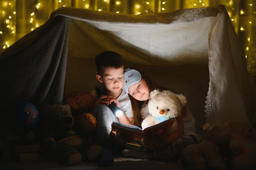happy family children reading a book with a flashlight in a tent at home photo