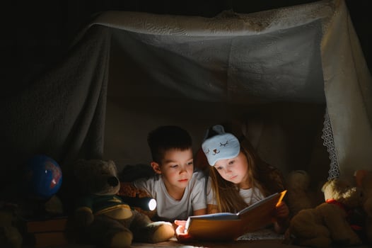 reading and family games in children's tent. boy and girl with book and flashlight before going to bed photo