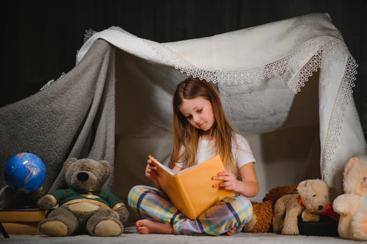 child girl reading with book and flashlight and teddy bear in tent. before going to bed photo