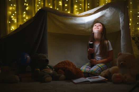 happy child girl laughing and reading book in dark in a tent at home photo