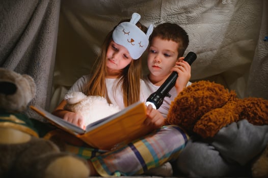 reading and family games in children's tent. boy and girl with book and flashlight before going to bed photo