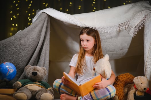 Little girl are reading a book with flashlights in tent. Happy girl playing at home. Funny lovely kid having fun in room. photo