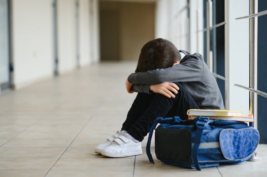 Upset boy sitting at school and crying after bullying by pupils classmates. The child covered his face with his hands and cries photo