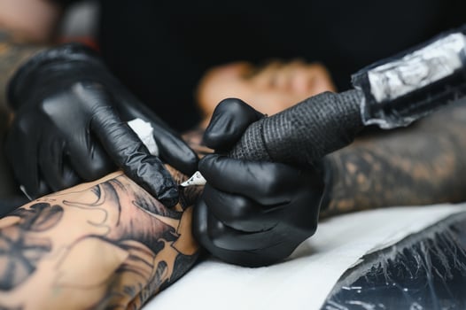 Cropped close up of a bearded tattoo artist working at his studio tattooing sleeve on the arm of his male client. Man getting tattooed by professional tattooist photo