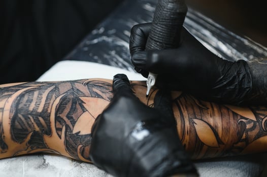 Cropped close up of a bearded tattoo artist working at his studio tattooing sleeve on the arm of his male client. Man getting tattooed by professional tattooist photo