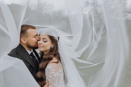 a handsome and stylish groom embraces his bride in a white dress under her veil photo