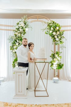 A bride and groom stand in front of a cake on a table photo