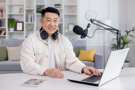 Portrait of blogger at home, Asian man smiling and looking at camera, man sitting at table with laptop in living room, recording audio podcasts and doing online radio. photo