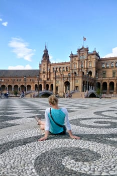 Back view of solo traveler girl sitting on the square of Spain in Seville. Backview of woman tourist in Sevilla trip. Solo vacation concept. photo