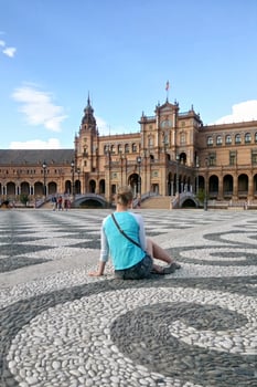 Back view of solo traveler girl sitting on the square of Spain in Seville. Backview of woman tourist in Sevilla trip. Solo vacation concept. photo
