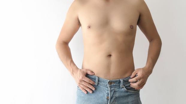 Adult man with partially toned abdomen, shirtless, wearing blue jeans, white background, and space for text. photo