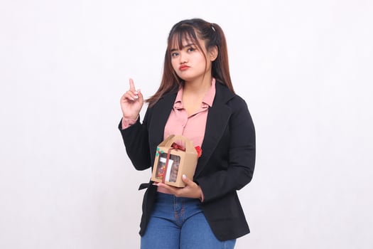 Beautiful Asian girl in her 20s pouting excitedly pointing up Christmas gift in the form of hamper in hand on white background for advertising materials, banners, billboards photo