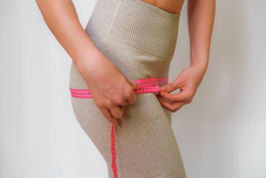 Cropped view of slim woman measuring hips with tape measure at home, close up. An unrecognizable European woman checks the result of a weight loss diet or liposuction indoors. Healthy lifestyle. photo