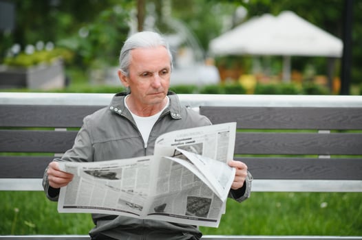 Handsome grandfather sits on a bench in the park and reads a newspaper. Senior gray-haired man. photo