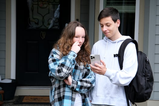 teenagers show interesting news boy and girl with briefcase phone at door at home Smiling couple looking in smartphone together. Beautiful loving couple laughing and watching something on mobile phone photo