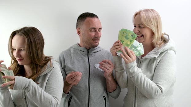 a man father and husband stand with money rejoicing in life daughter and wife come and take all money man spreads his arms to sides frustrated remains alone tracksuits Cheerful family dollars euros photo