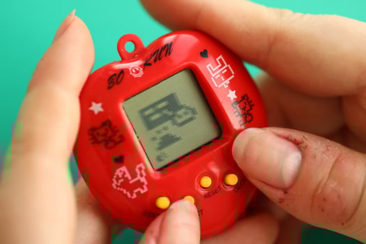 KYIV, UKRAINE - MARCH 9, 2024 Retro pet keychain game tamagotchi in red plastic case in female hands photo