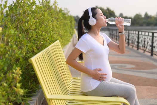 Beautiful pregnant woman drinking bottle of pure water in the park, Healthy and active pregnancy lifestyle concept. photo