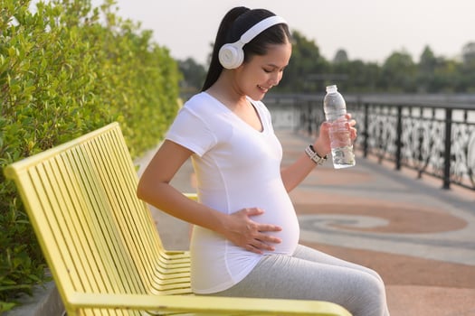 Beautiful pregnant woman drinking bottle of pure water in the park, Healthy and active pregnancy lifestyle concept. photo