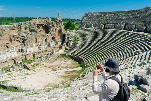 A male tourist enjoys a walk through the amphitheater among the ruins of the ancient city of Perge, in Turkey. The tourist looks around the ancient city of Perge with fascination and takes photographs photo