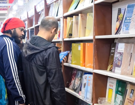 Delhi, India, February 17 2024 - Various age group people reading variety of Books on shelf inside a book-stall at Delhi International Book Fair, Books in Annual Book Fair at Bharat Mandapam complex photo