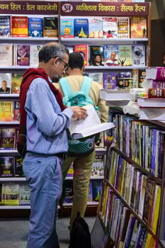 Delhi, India, February 17 2024 - Various age group people reading variety of Books on shelf inside a book-stall at Delhi International Book Fair, Books in Annual Book Fair at Bharat Mandapam complex photo