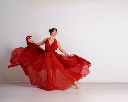 Dancer in a red flying dress. Woman ballerina dancing on a white studio background photo