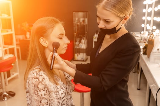 Makeup beauty salon. Makeup artist applies powder and blush. Beautiful female face. Makeup master's hand puts blush on cheeks of beauty model girl. Makeup in progress photo