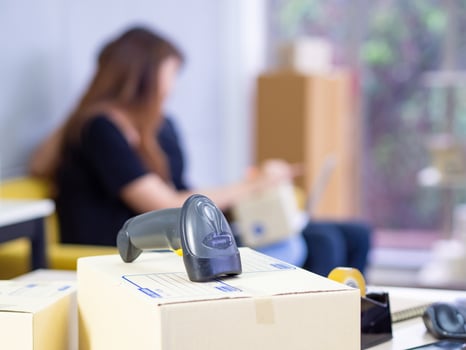 Close-up of reader barcode on parcel box in the office with young couple blurred background. Easy startup e-commerce and shipping service. Space for text. Business online concept photo