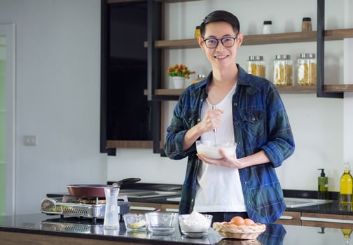 Young man cook wearing casual cloth in the kitchen. Young man worker uses whisk and bowl for making mixing ingredients in a bowl. Kitchen tools and cooking concept photo