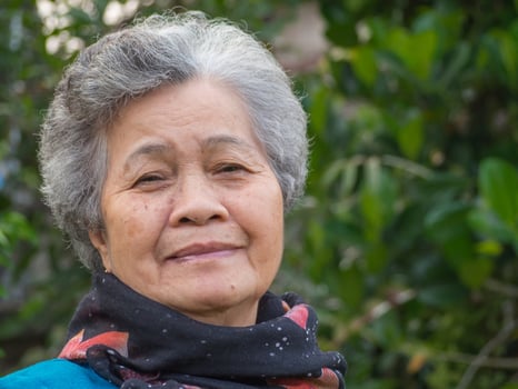 Portrait of a happy senior woman smiling and looking at the camera while standing against trees. Concept of aged people and healthcare photo