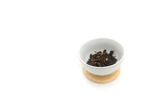 Dry black tea in round bowl isolated on white background photo