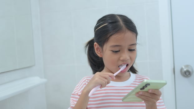 A young girl is brushing her teeth while looking at her phone photo