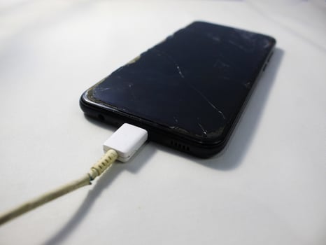 Old charger cable broken and smartphone, Defective charging cord, Connection deterioration device photo