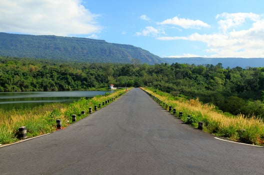 The road stretches along a beautiful river or lake, with mountains, blue sky, white cloud and green forests in the foreground at Wang Bon reservoir, Nakhon Nayok, Thailand. photo